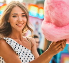 kobieta w wieku 25 plus w sukience w groszki i z wielką watą cukrową uśmiecha się szeroko