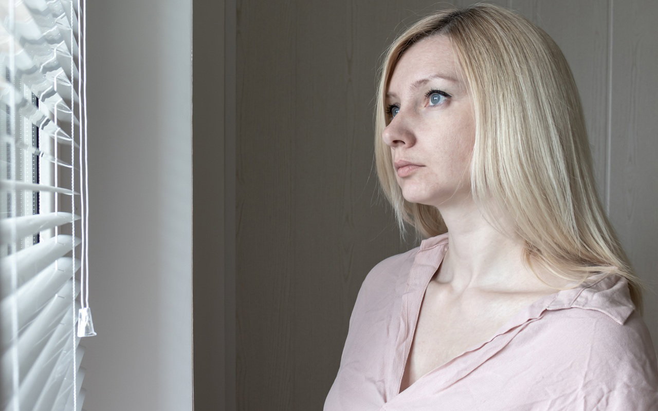 kobieta w wieku 30 plus blondynka stoi przy oknie smutna i zamyślona
