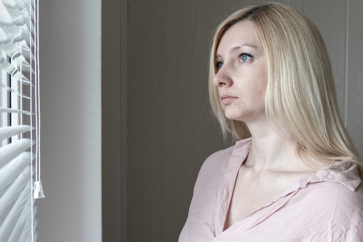 kobieta w wieku 30 plus blondynka stoi przy oknie smutna i zamyślona