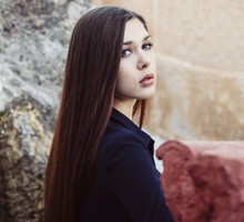 kobieta w wieku 30 plus z długimi włosami stoi na tle greckich murów zamyślona i smutna