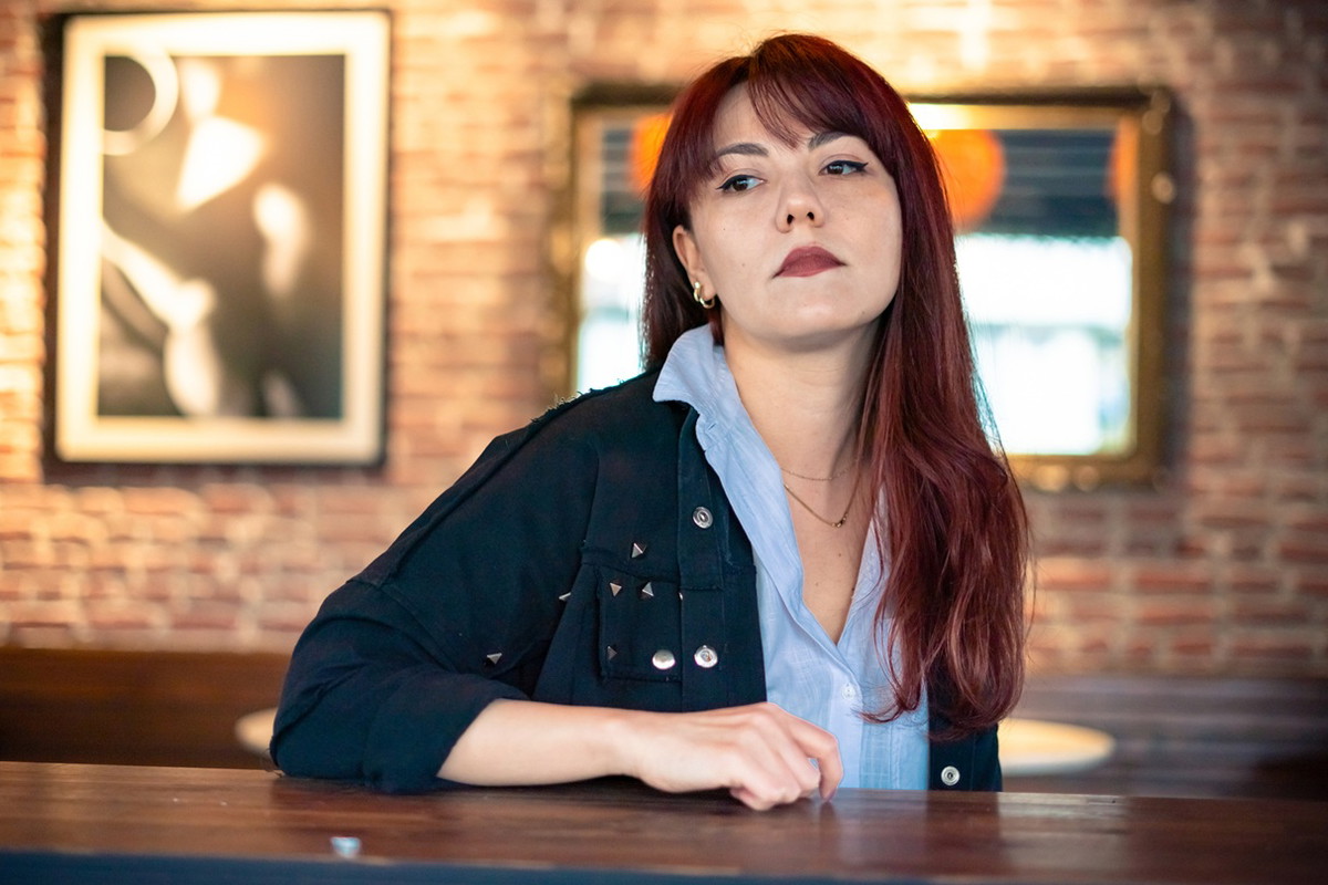kobieta w wieku 30 plus z kasztanowymi długimi włosamisiedzi w restauracji ze zdegustowaną miną na tle ściany z obrazami