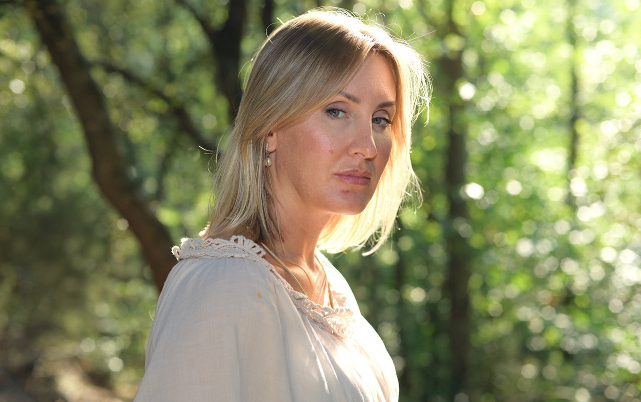 kobieta w wieku 40 plus blondynka stoi na tle zieleni ze smutną i zamyśloną miną