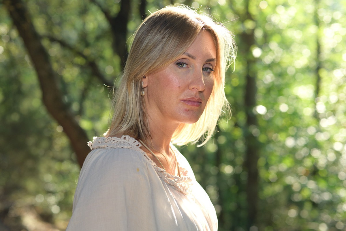 kobieta w wieku 40 plus blondynka stoi na tle zieleni ze smutną i zamyśloną miną