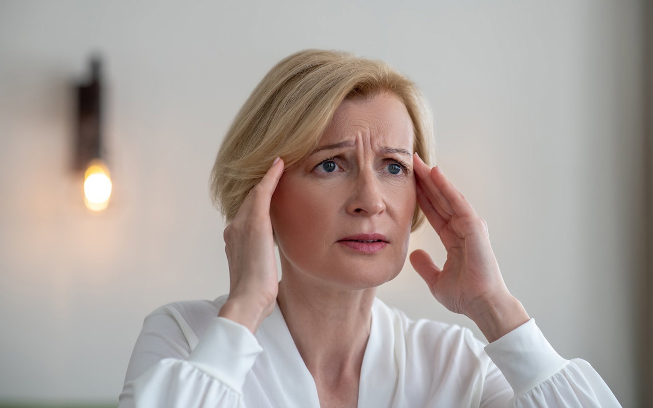 kobieta w wieku 50 plus blondynka w białej bluzce stoi zmarwiona i zrozpaczona w salonie