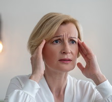 kobieta w wieku 50 plus blondynka w białej bluzce stoi zmarwiona i zrozpaczona w salonie