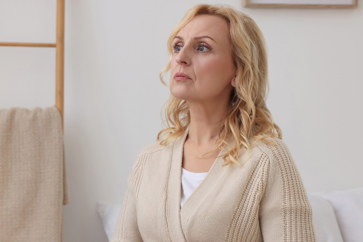 kobieta w wieku 55 plus blondynka w beżowym swetrze siedzi w pokoju lekko przerażona