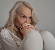 kobieta w wieku 55 plus jasne włosy siedzi na kanapie zdenerwowana i załamana