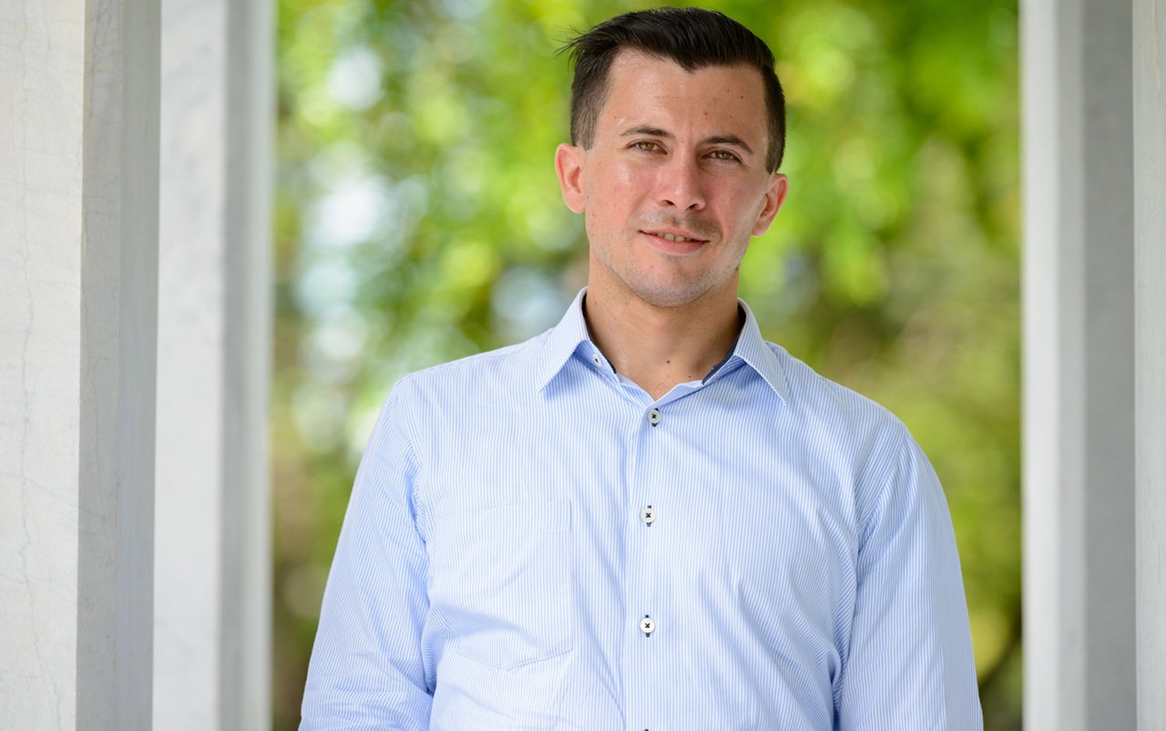 mężczyzna w wieku 35 plus w jasnej koszuli stoi na tle tarasu z nerwowym uśmiechem