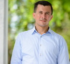 mężczyzna w wieku 35 plus w jasnej koszuli stoi na tle tarasu z nerwowym uśmiechem