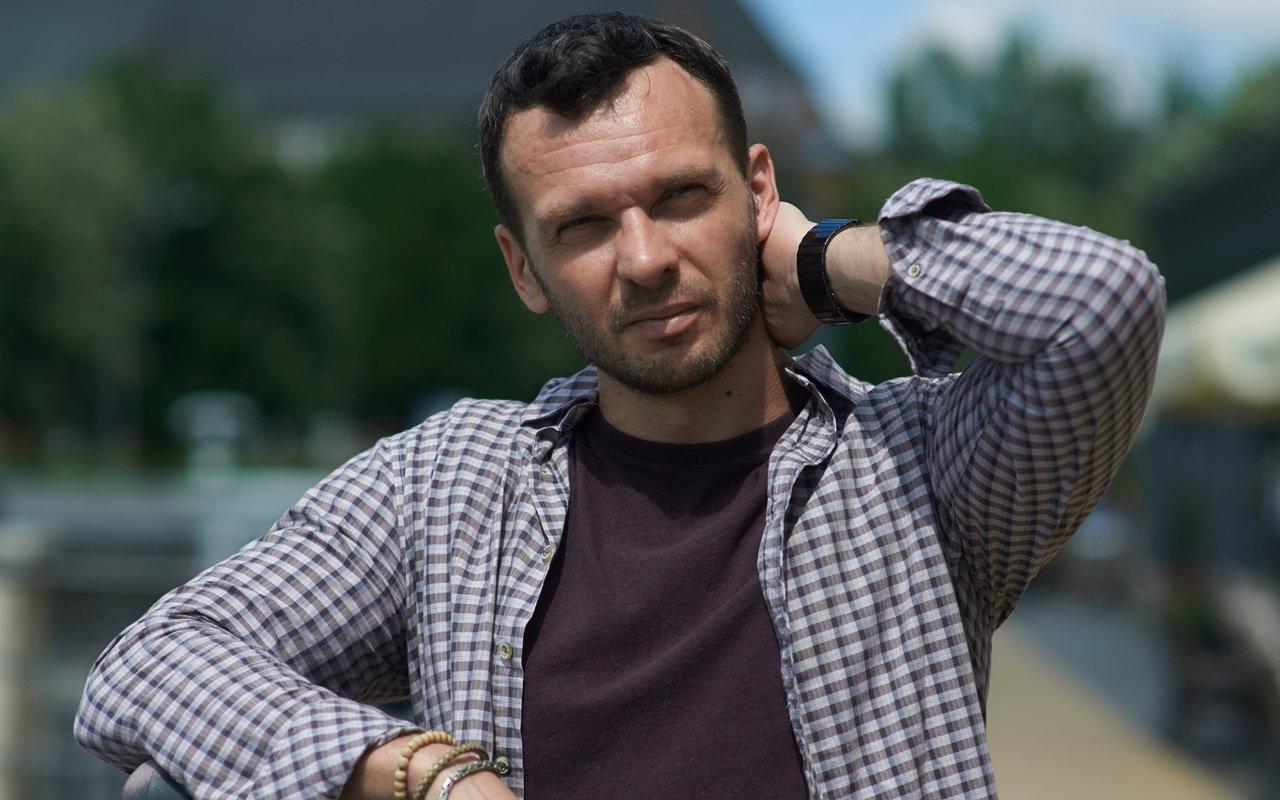 mężczyzna w wieku 35 plus w kraciastej koszuli stoi na ulicy w słońcu zamyślony