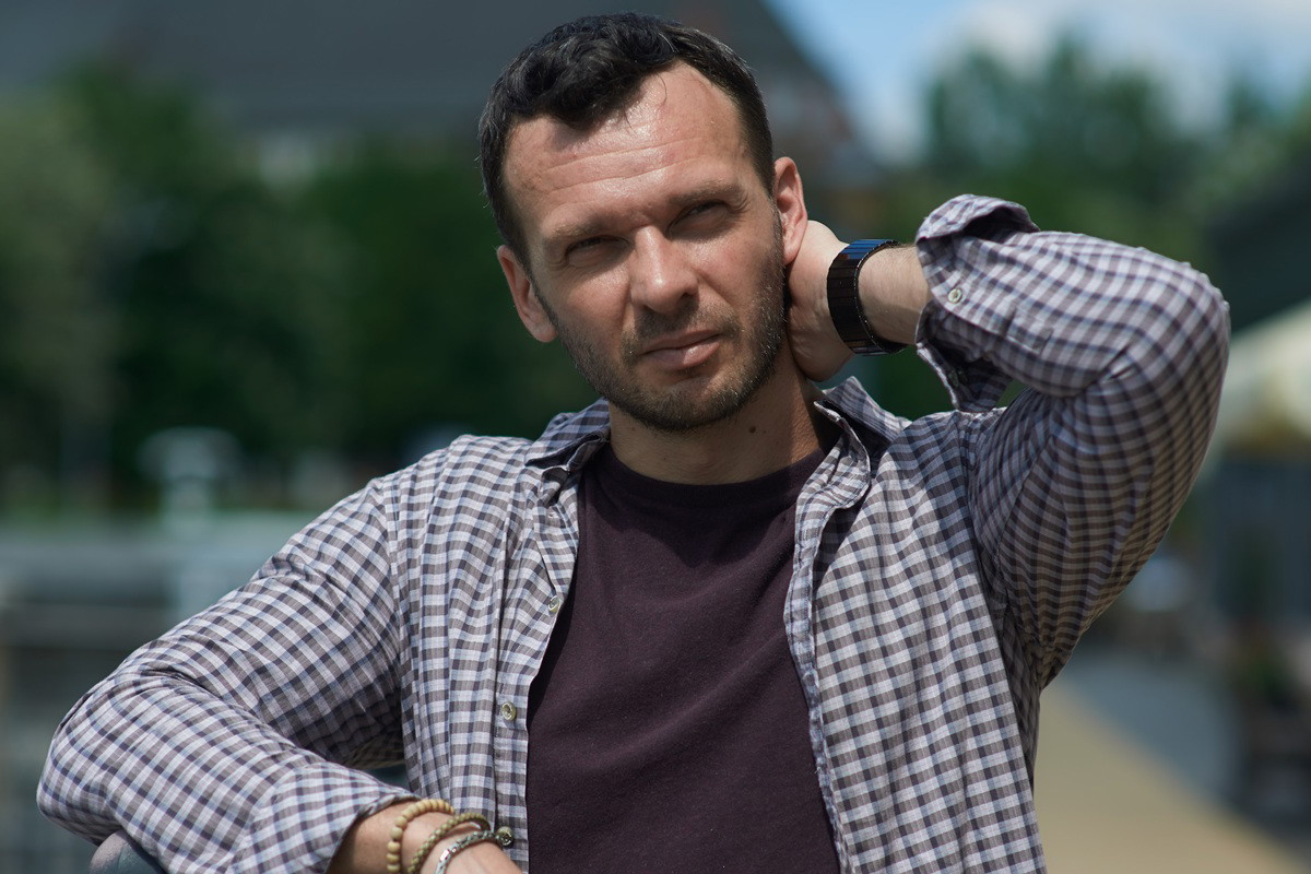 mężczyzna w wieku 35 plus w kraciastej koszuli stoi na ulicy w słońcu zamyślony