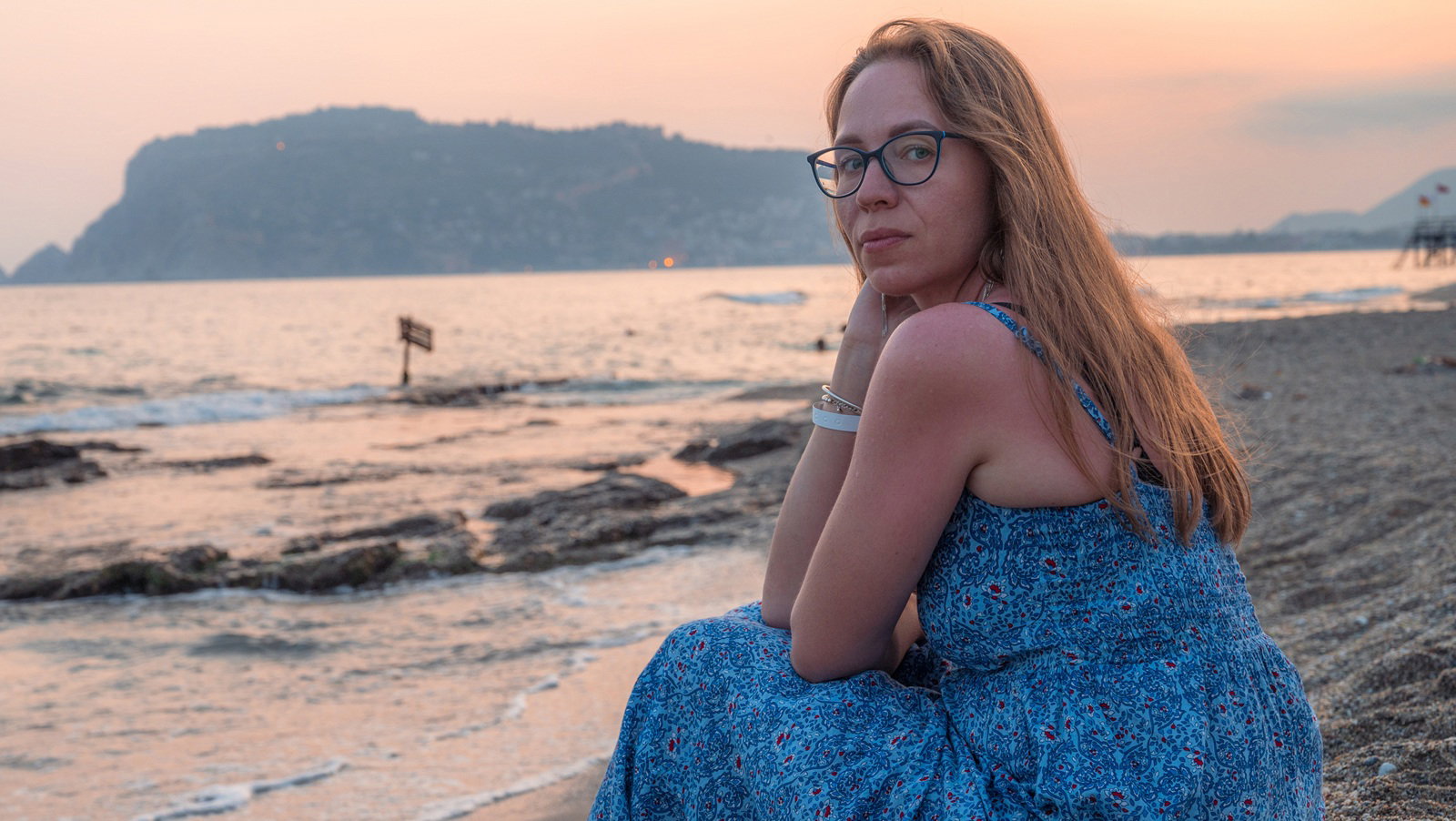kobieta 40 plus w okularach siedzi na plaży przy zachodzącym słońcu w Turcji w Alanyi zamyślona i smutna