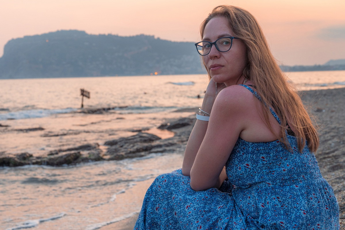 kobieta 40 plus w okularach siedzi na plaży przy zachodzącym słońcu w Turcji w Alanyi zamyślona i smutna