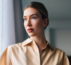kobieta w wieku 30 plus blondynka w koszuli bez rękawów stoi zamyślona na tle okna i salonu