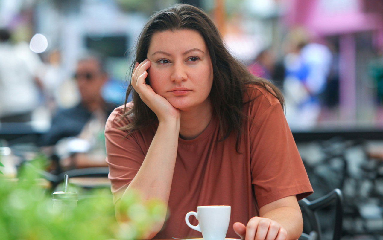 kobieta w wieku 35 plus siedzi przy stoliku w kawiarni na zewnątrz na tle ulicy i smutno rozmyśla