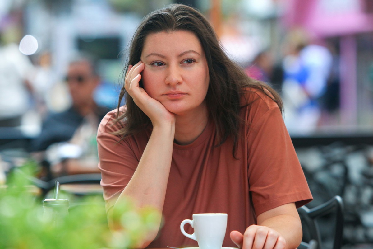 kobieta w wieku 35 plus siedzi przy stoliku w kawiarni na zewnątrz na tle ulicy i smutno rozmyśla
