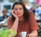 kobieta w wieku 35 plus siedzi przy stoliku w kawiarni na zewnątrz na tle ulicy i smutno rozmyśla