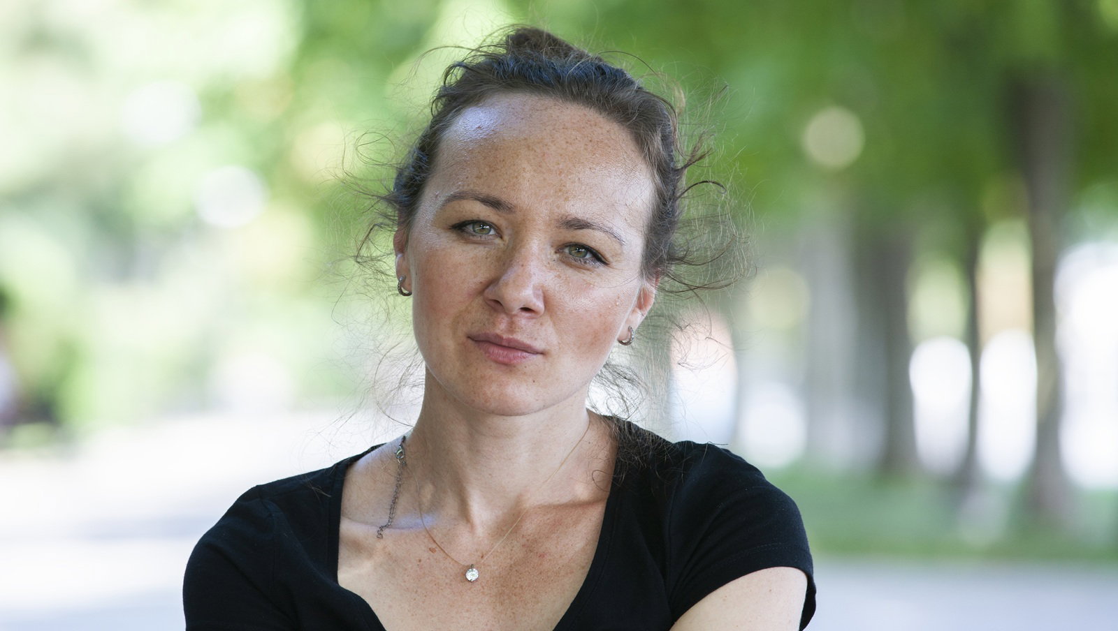 kobieta w wieku 35 plus w czarnej koszulce siedzi na tle zieleni z poważną miną letnią porą