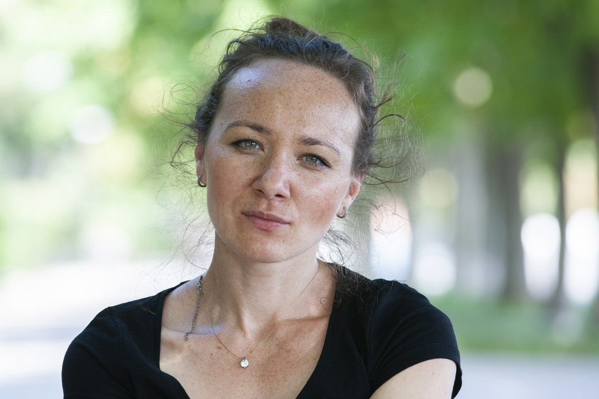 kobieta w wieku 35 plus w czarnej koszulce siedzi na tle zieleni z poważną miną letnią porą