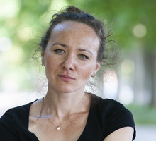 kobieta w wieku 35 plus w czarnej koszulce siedzi na tle zieleni z poważną miną letnią porą