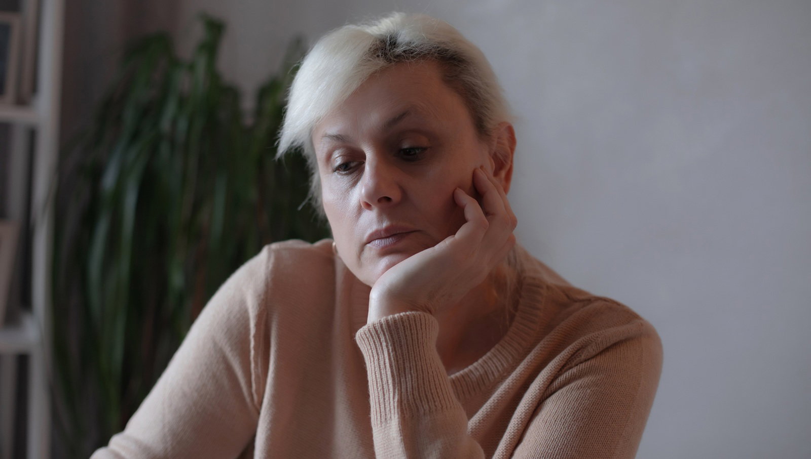 kobieta w wieku 40 plus blondynka tleniona siedzi przy stole w salonie zamyślona i smutna