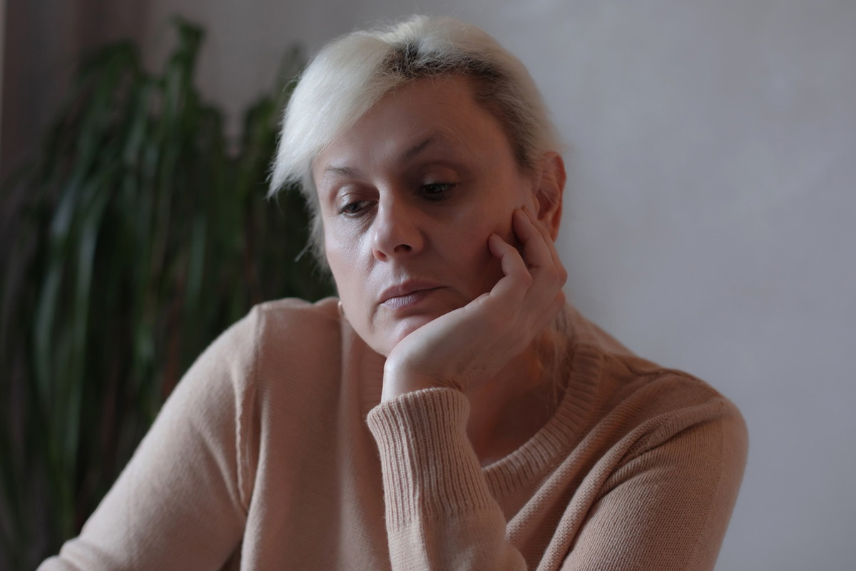 kobieta w wieku 40 plus blondynka tleniona siedzi przy stole w salonie zamyślona i smutna