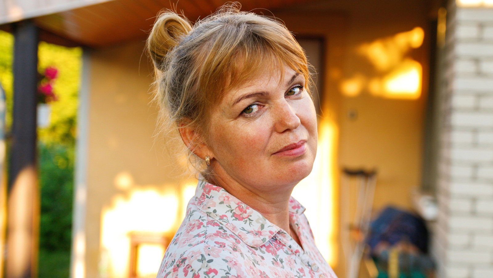 kobieta w wieku 45 plus blondynka ze spiętymi włosami stoi na tle tarasu z lekko kpiącą miną