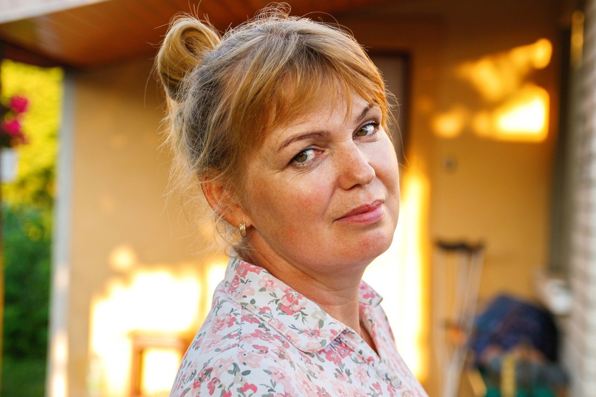 kobieta w wieku 45 plus blondynka ze spiętymi włosami stoi na tle tarasu z lekko kpiącą miną