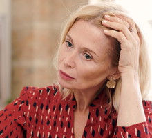 kobieta w wwieku 50 plus blondynka w czerwonej wzorzystej sukience siedzi przy stole załamana i zamyślona