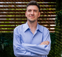 mężczyzna w wieku 35 plus w niebieskiej koszuli stoi na tle altany z poważną miną zamyślony
