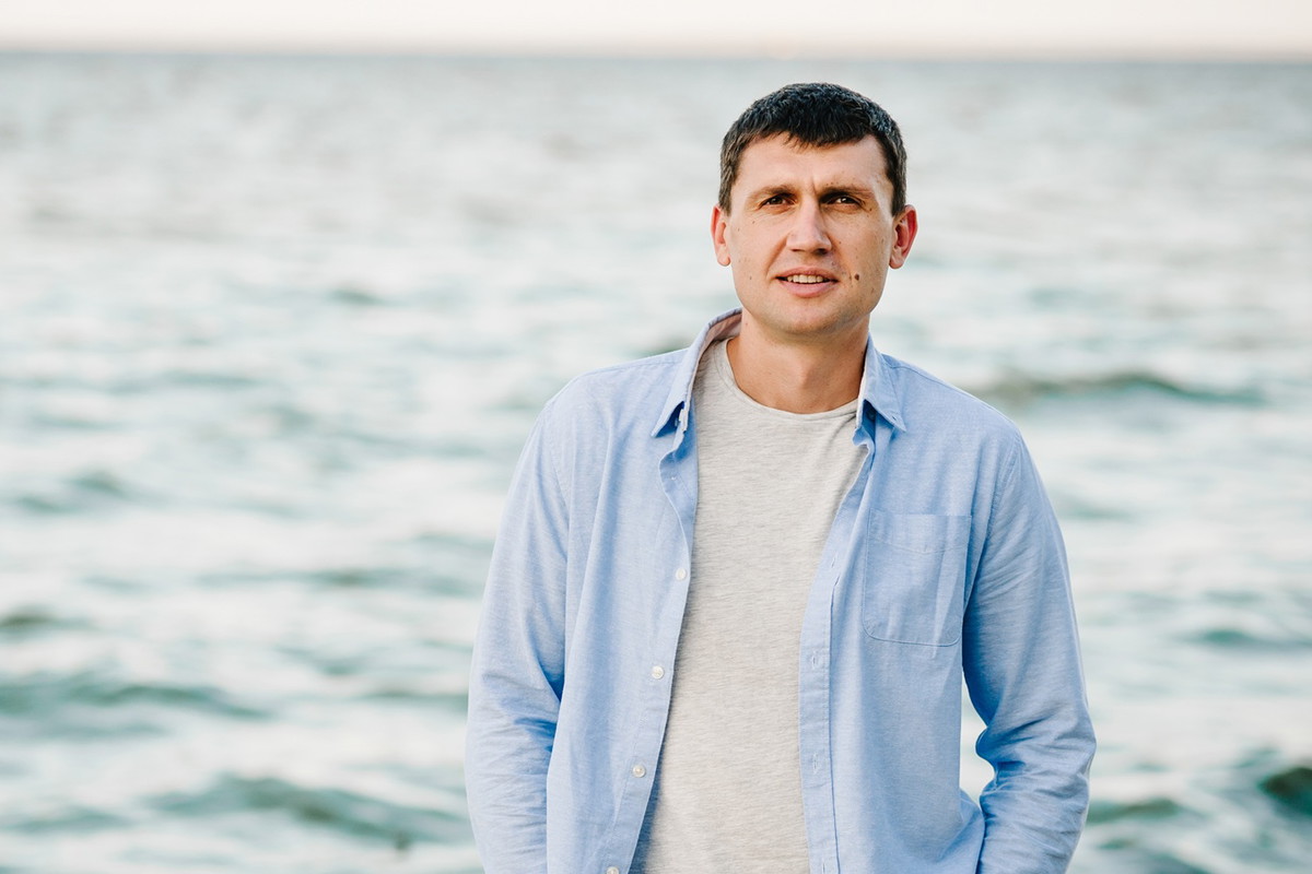mężczyzna w wieku 40 plus stoi na plaży w niebieskiej koszuli z poważną miną
