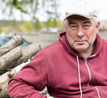 mężczyzna w wieku 60 plus w czapce i czerwonej bluzie siedzi na podwórku smutny i zamyślony