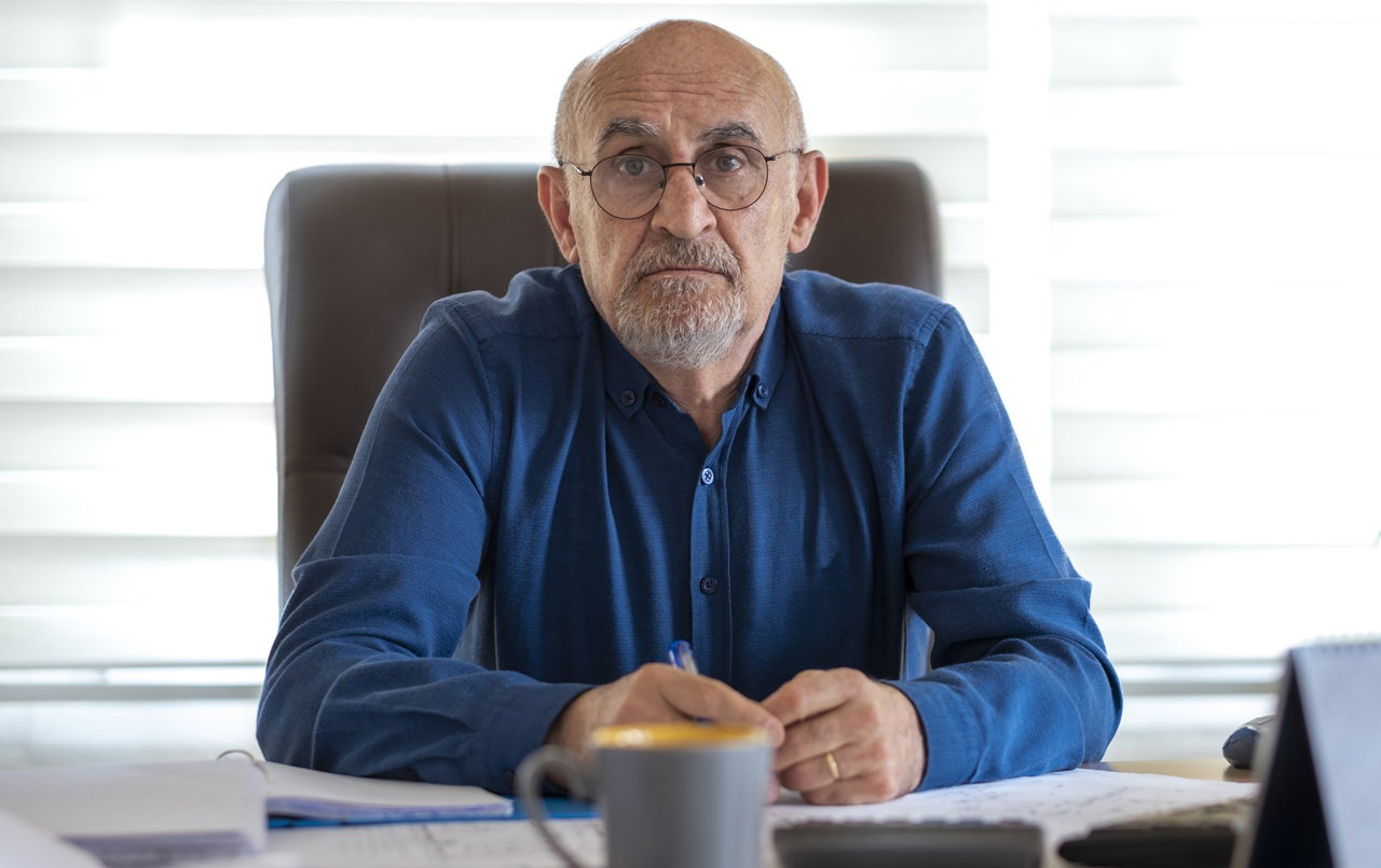 mężczyzna w wieku 60 plus z brodą i wąsami w okularach w niebieskiej koszuli siedzi z rozczarowaną i smutna miną