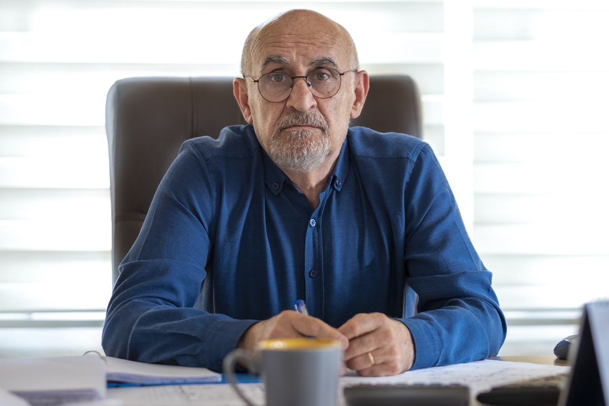 mężczyzna w wieku 60 plus z brodą i wąsami w okularach w niebieskiej koszuli siedzi z rozczarowaną i smutna miną