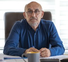 mężczyzna w wieku 60 plus z brodą i wąsami w okularach w niebieskiej koszuli siedzi z rozczarowaną i smutna miną