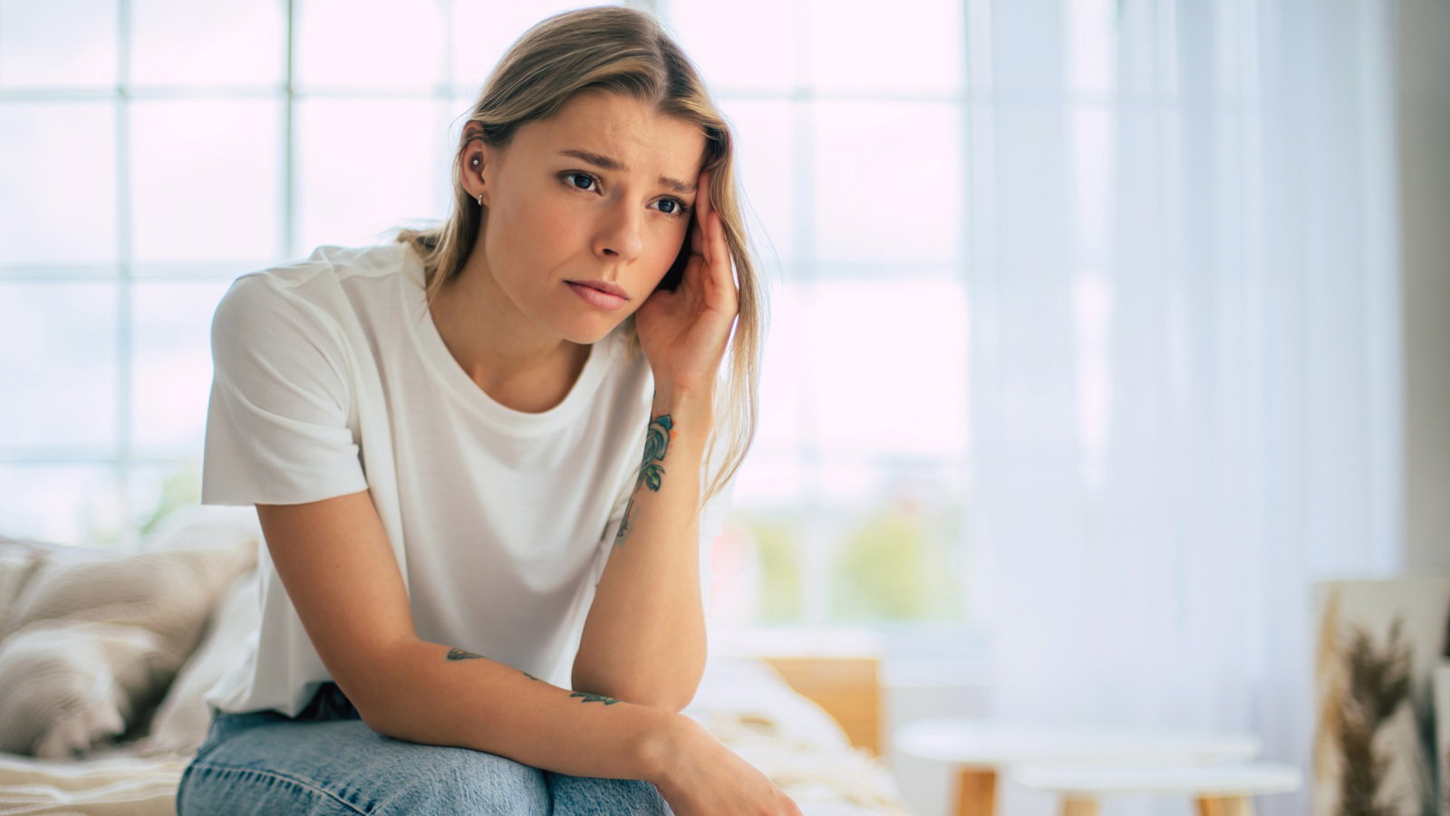 kobieta w wieku 25 plus blondynka w białym t-shircie siedzi w pokoju ze zmartwioną miną