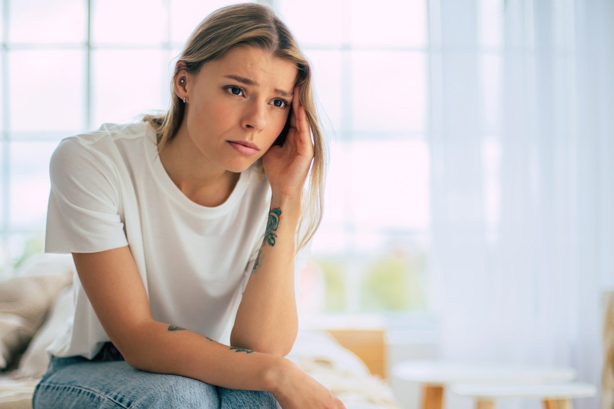 kobieta w wieku 25 plus blondynka w białym t-shircie siedzi w pokoju ze zmartwioną miną