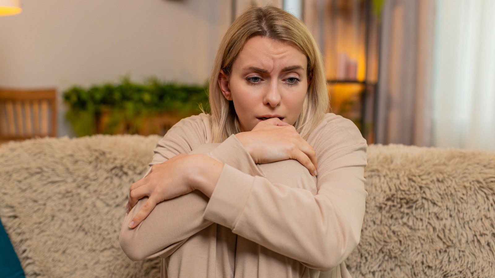 kobieta w wieku 30 plus blondynka w beżowym dresie siedzi na kanapie załamana i smutna