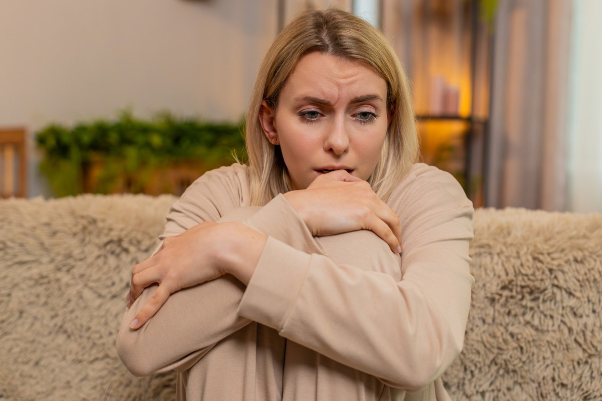 kobieta w wieku 30 plus blondynka w beżowym dresie siedzi na kanapie załamana i smutna