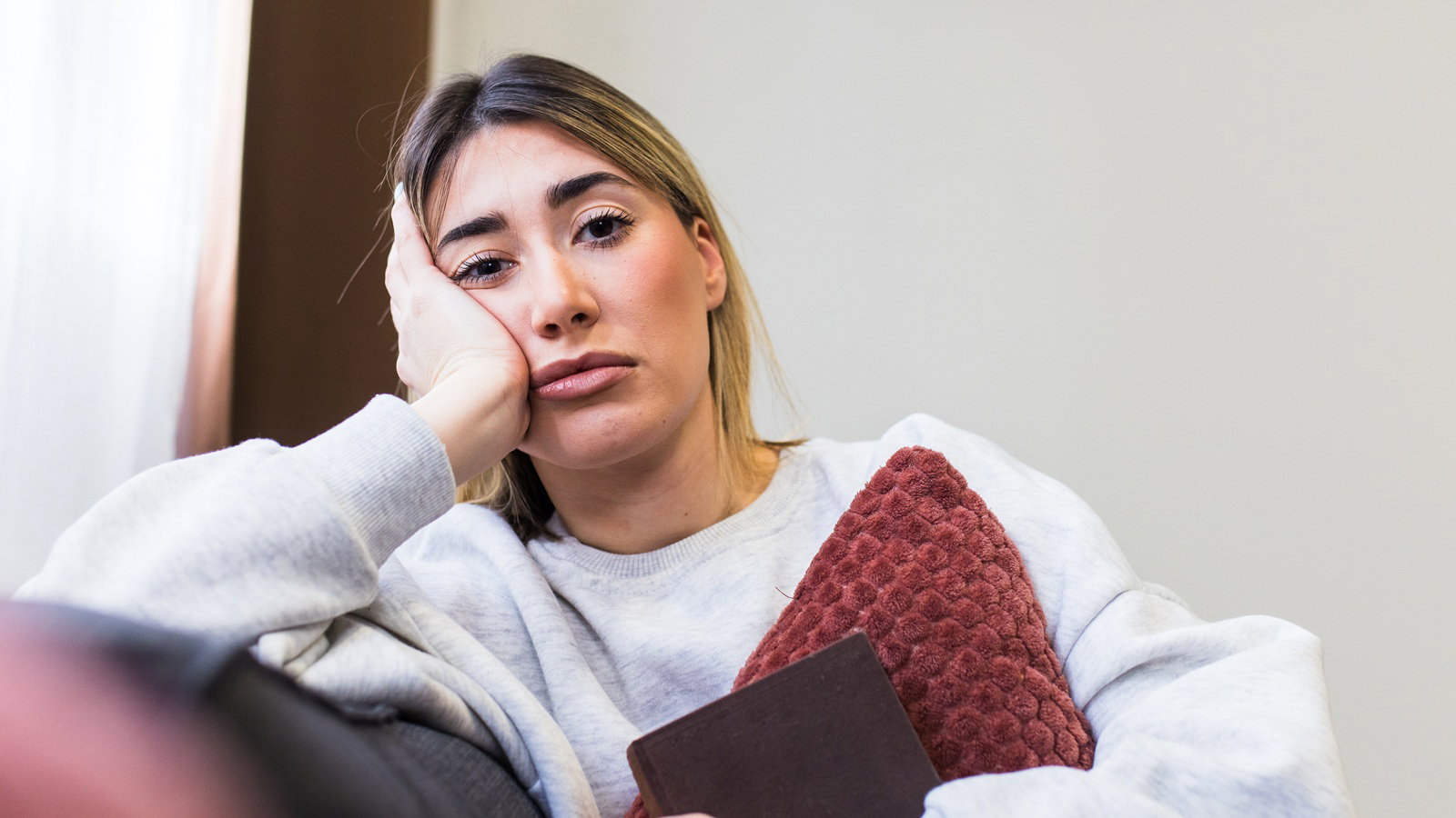 kobieta w wieku 30 plus siedzi na kanapie ściskając poduszkę z rozczarowaną miną