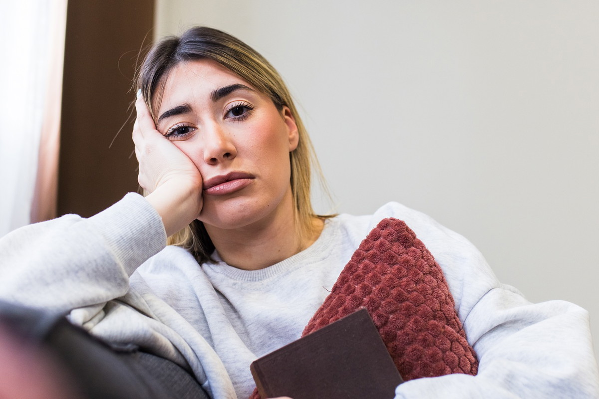 kobieta w wieku 30 plus siedzi na kanapie ściskając poduszkę z rozczarowaną miną