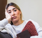 kobieta w wieku 30 plus siedzi na kanapie ściskając poduszkę z rozczarowaną miną