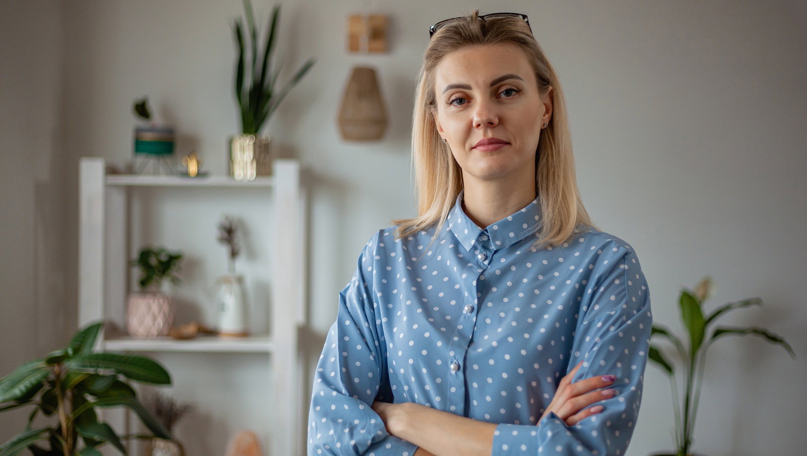 kobieta w wieku 30 plus w niebieskiej koszuli w groszki blond włosy stoi z poważną miną w pokoju