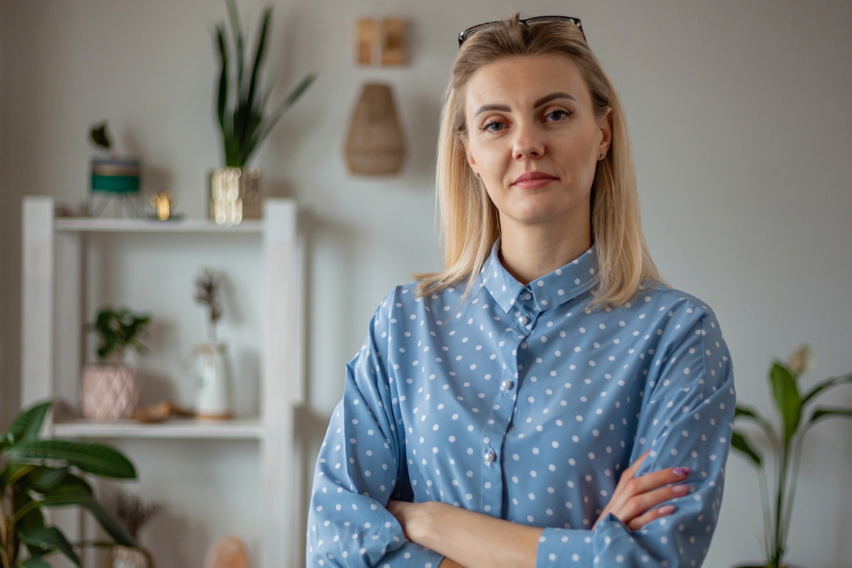 kobieta w wieku 30 plus w niebieskiej koszuli w groszki blond włosy stoi z poważną miną w pokoju