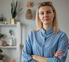kobieta w wieku 30 plus w niebieskiej koszuli w groszki blond włosy stoi z poważną miną w pokoju