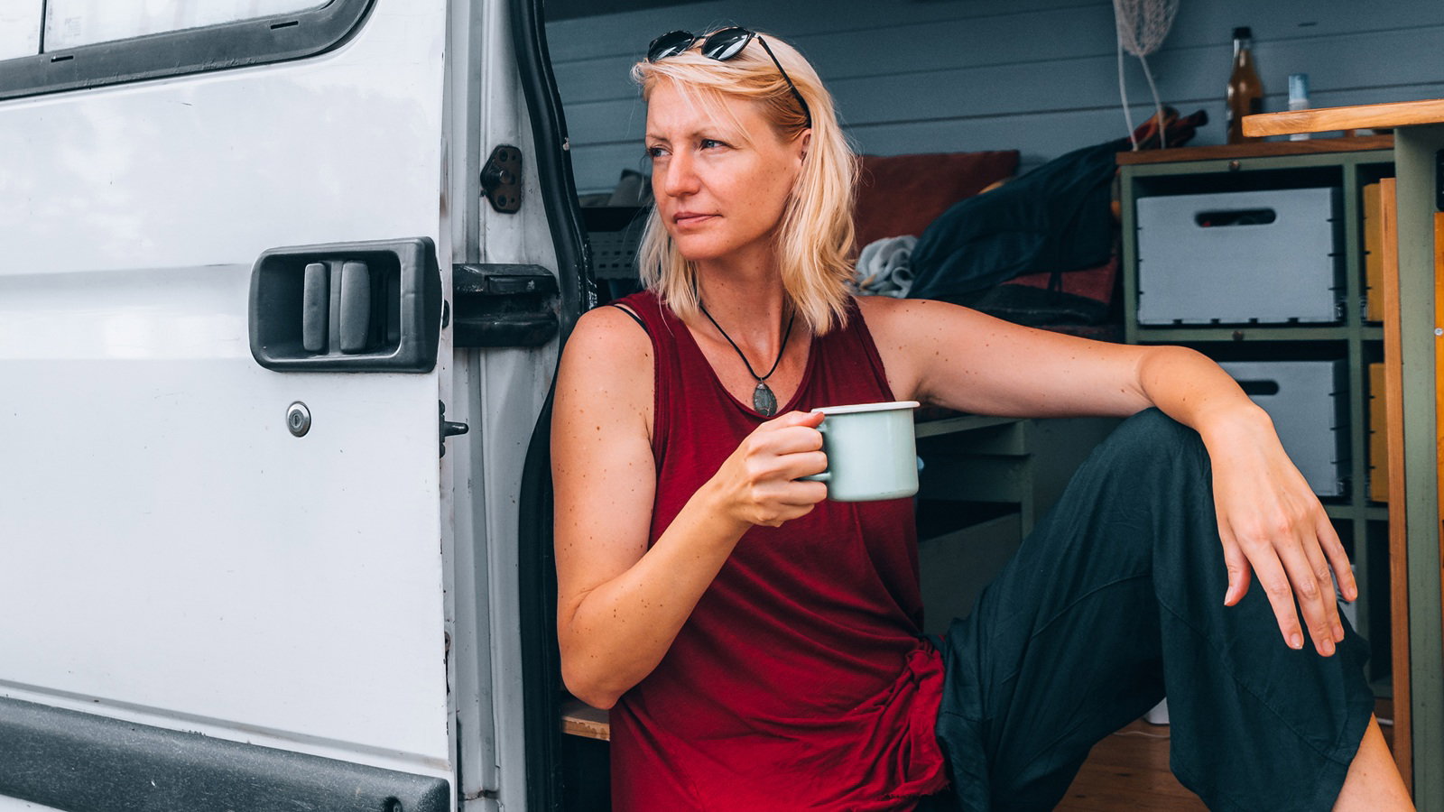 kobieta w wieku 35 plus blondynka w czerwonej bluzce siedzi w kamperze z kubkiem herbaty w ręku zamyślona