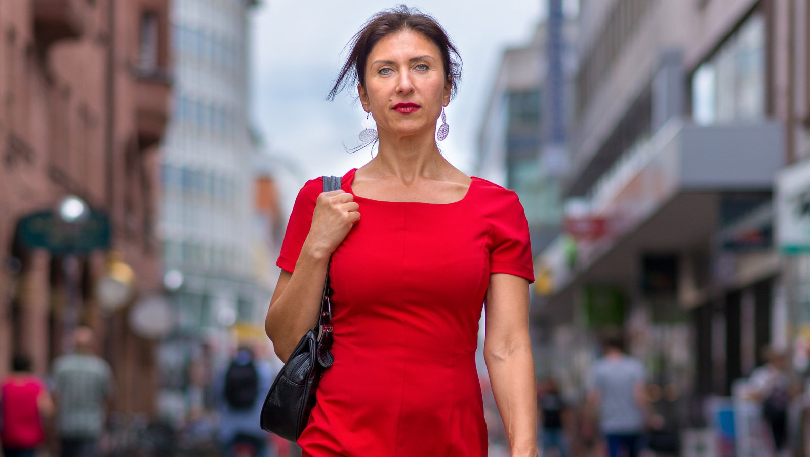 kobieta w wieku 40 plus w czerwonej sukience idzie po ulicy z poważną dumną miną