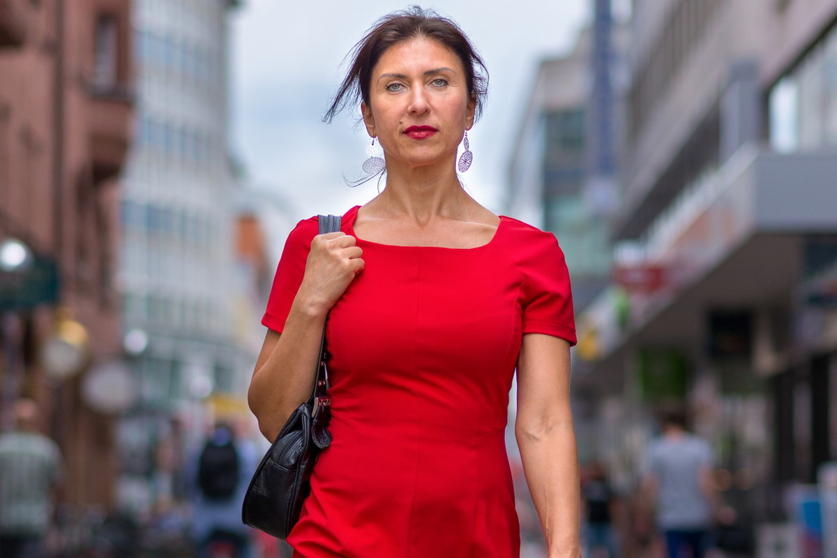 kobieta w wieku 40 plus w czerwonej sukience idzie po ulicy z poważną dumną miną
