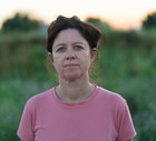 kobieta w wieku 40 plus w różowym t-shircie stoi na tle zachodzącego słońca na wsi zamyślona
