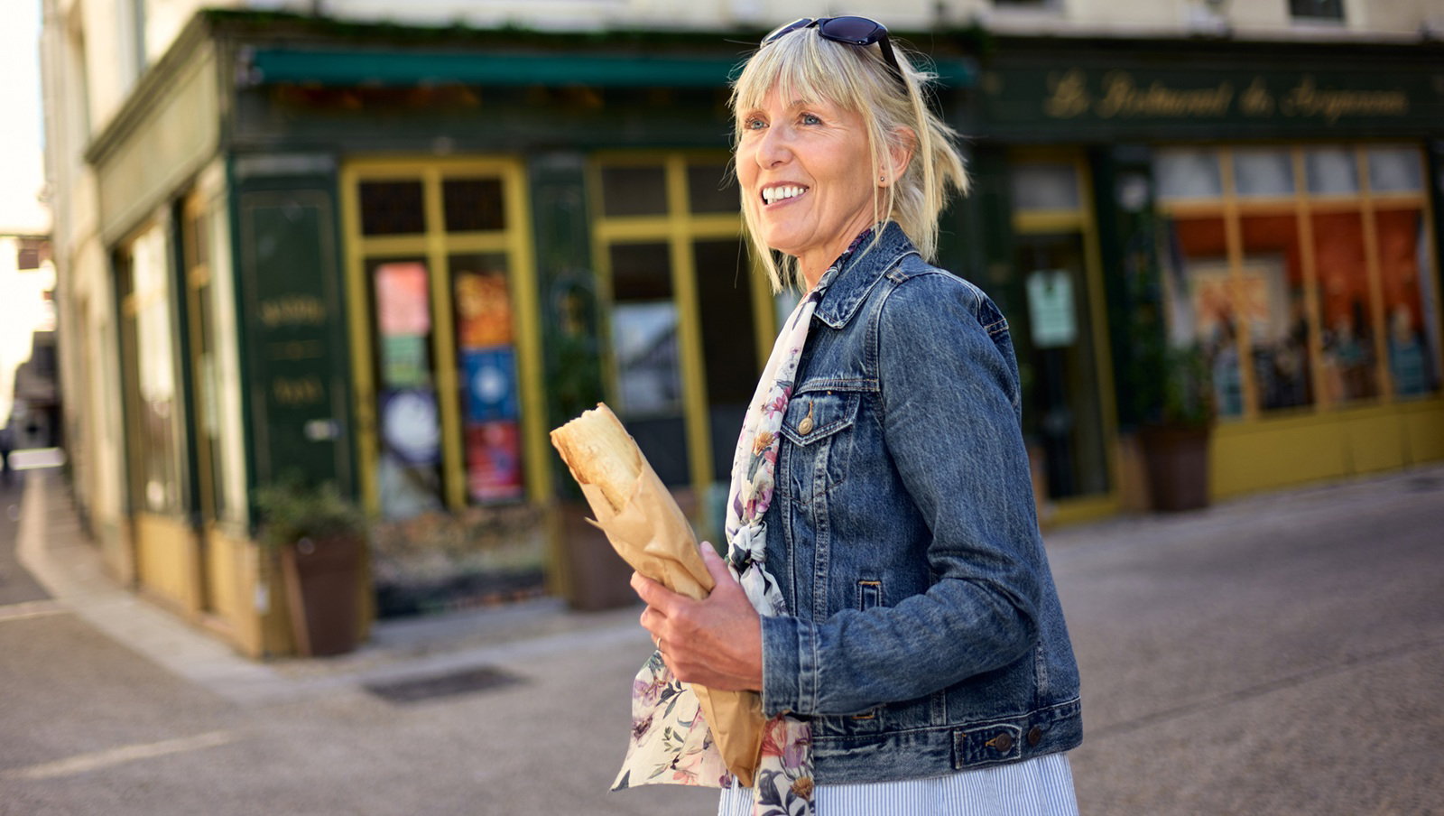 kobieta w wieku 50 plus blondynka w jeansowej kurtce stoi w Avignon w Prowansji we Francji z bagietką i uśmiecha się